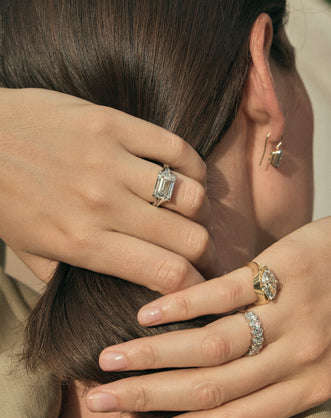 Model wears Perry East-West 5ct emerald solitaire double band engagement ring in 18ct white gold