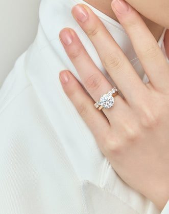 Model wears Cambon round brilliant six claw solitaire swept shoulder engagement ring in 18ct yellow gold
