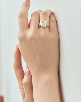 Model wears Rivington 5ct asscher signet bezel grooved band engagement ring in 18ct yellow gold