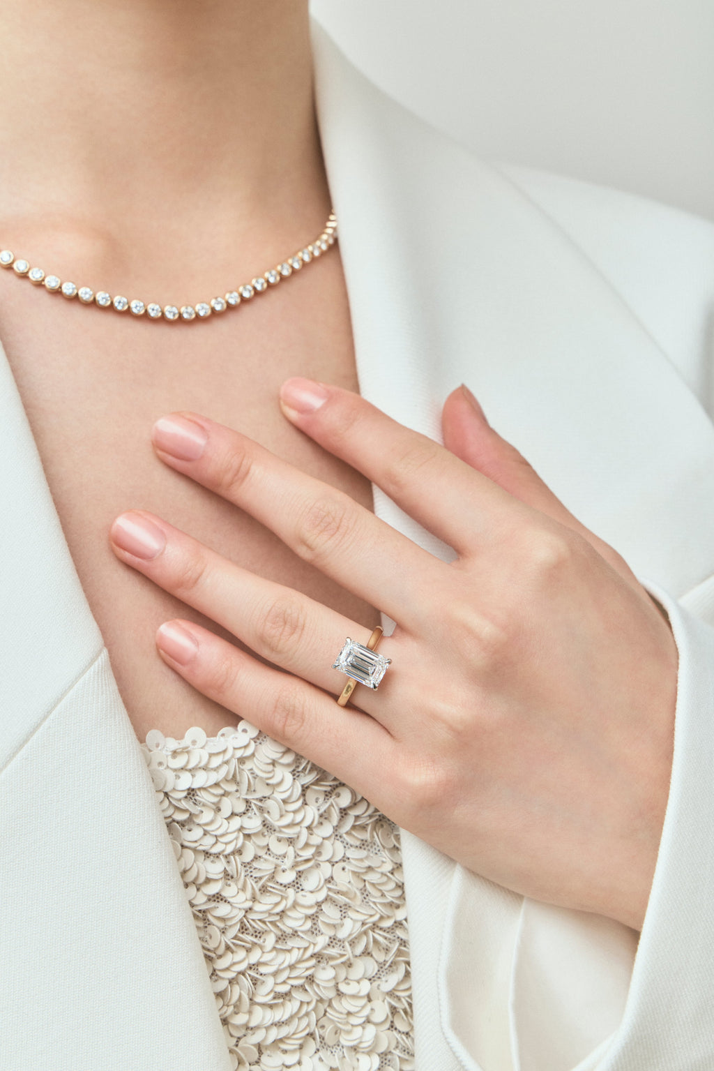 Model wears Dover emerald cut solitaire swept shoulder engagement ring in 18ct yellow gold
