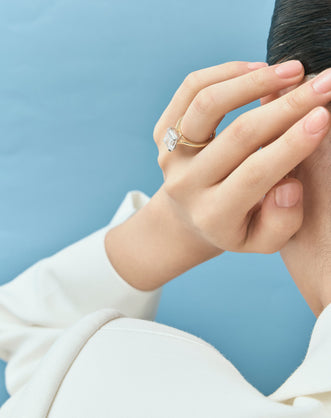 Model wears Dover emerald cut solitaire swept shoulder engagement ring in 18ct yellow gold