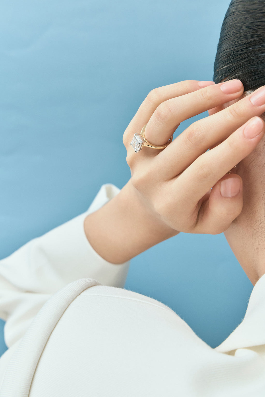 Model wears Dover emerald cut solitaire swept shoulder engagement ring in 18ct yellow gold