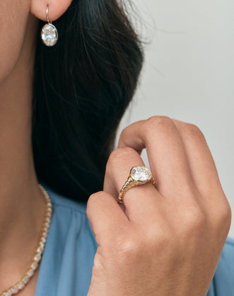 Model wears Chrystie 3ct round brilliant signet bezel grooved band engagement ring in 18ct yellow gold