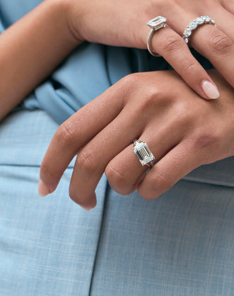 Model wears Perry East-West 5ct emerald solitaire double band engagement ring in 18ct white gold