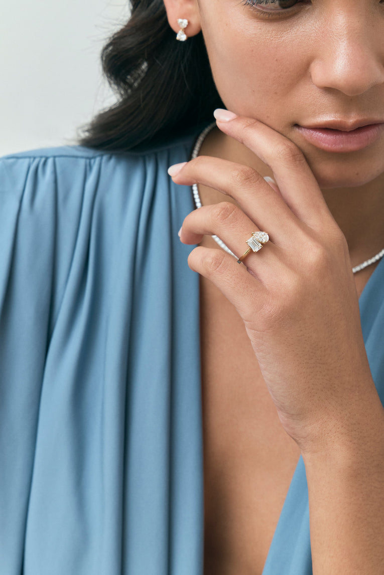 Close-up model wears Kinney Toi Et Moi pear emerald engagement ring in 18ct yellow gold