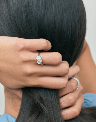 Close-up model wears Kinney Toi Et Moi pear emerald engagement ring in 18ct yellow gold