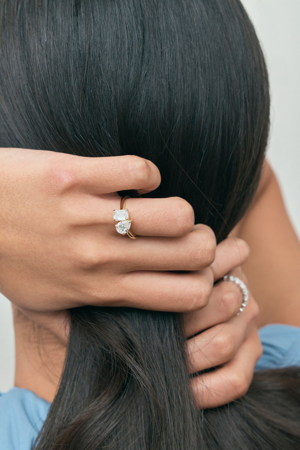Close-up model wears Kinney Toi Et Moi pear emerald engagement ring in 18ct yellow gold
