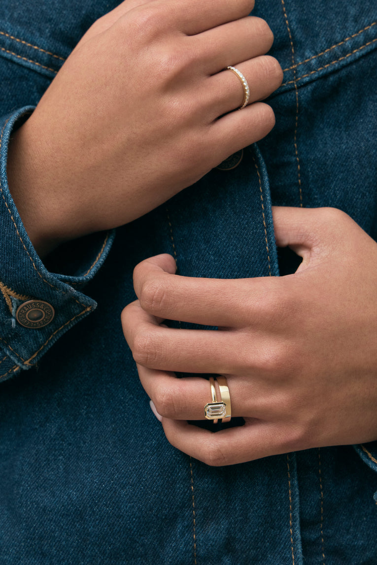 Model wears Sutton emerald cut solitaire bezel north-south engagement ring in 18ct yellow gold