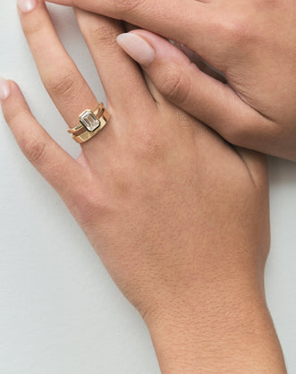 Model wears Sutton emerald cut solitaire bezel north-south engagement ring in 18ct yellow gold