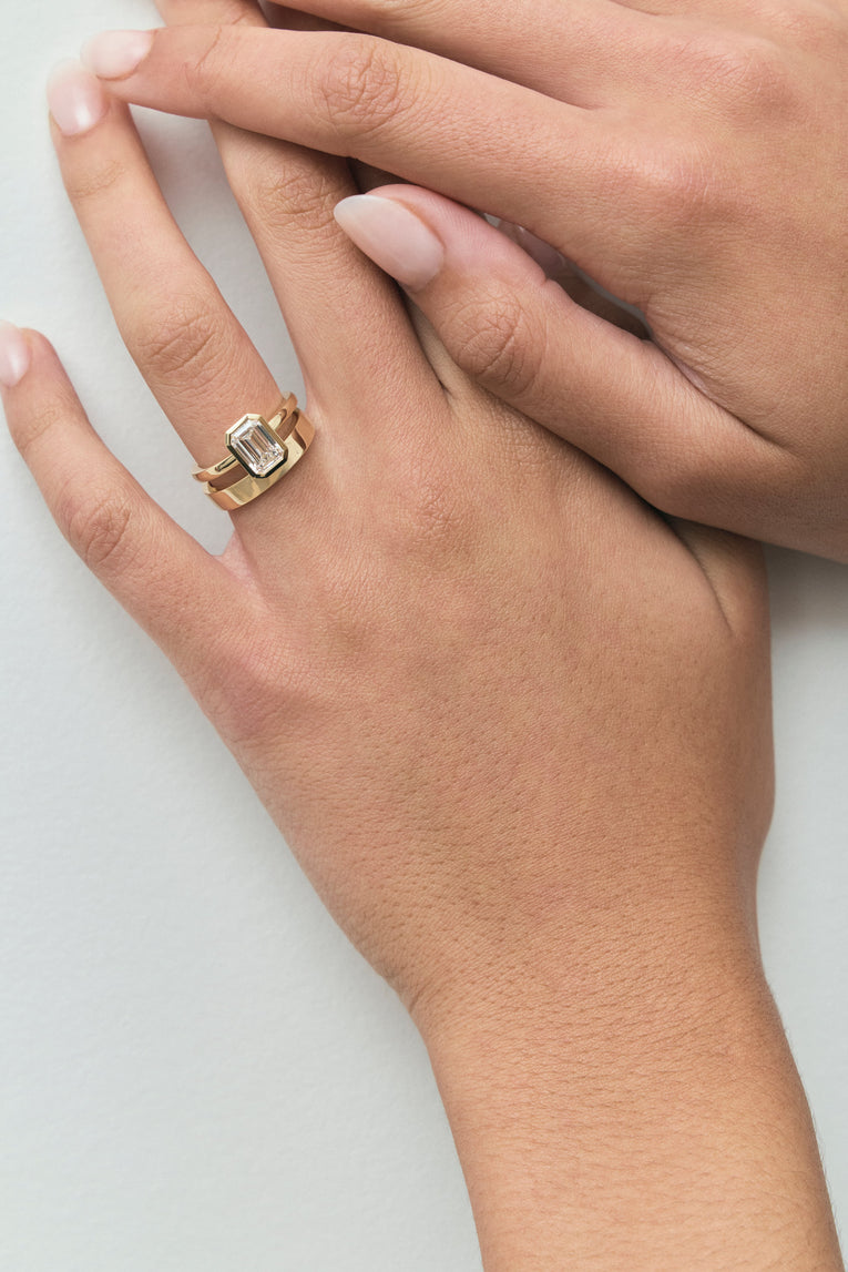 Model wears Sutton emerald cut solitaire bezel north-south engagement ring in 18ct yellow gold