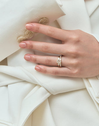 Close-up model wears Bruton emerald cut pear side stone engagement ring in 18ct yellow gold