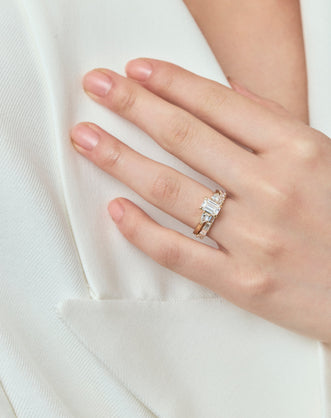 Close-up model wears Bruton emerald cut pear side stone engagement ring in 18ct yellow gold