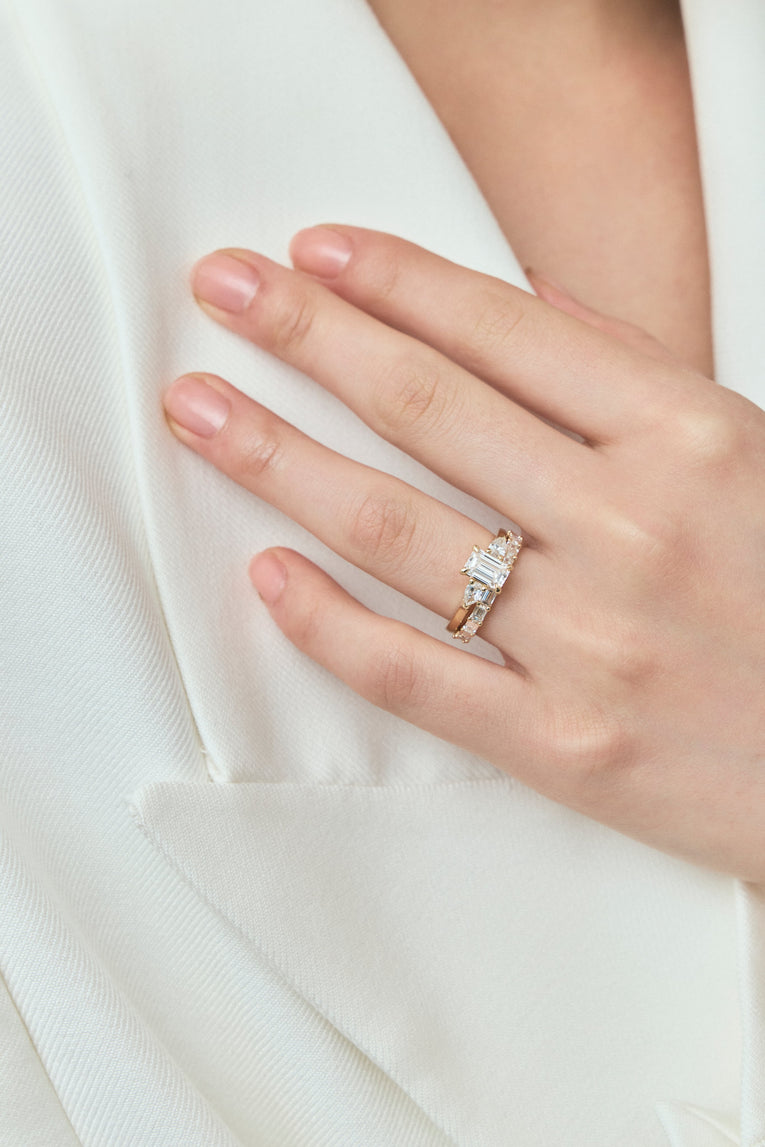 Close-up model wears Bruton emerald cut pear side stone engagement ring in 18ct yellow gold