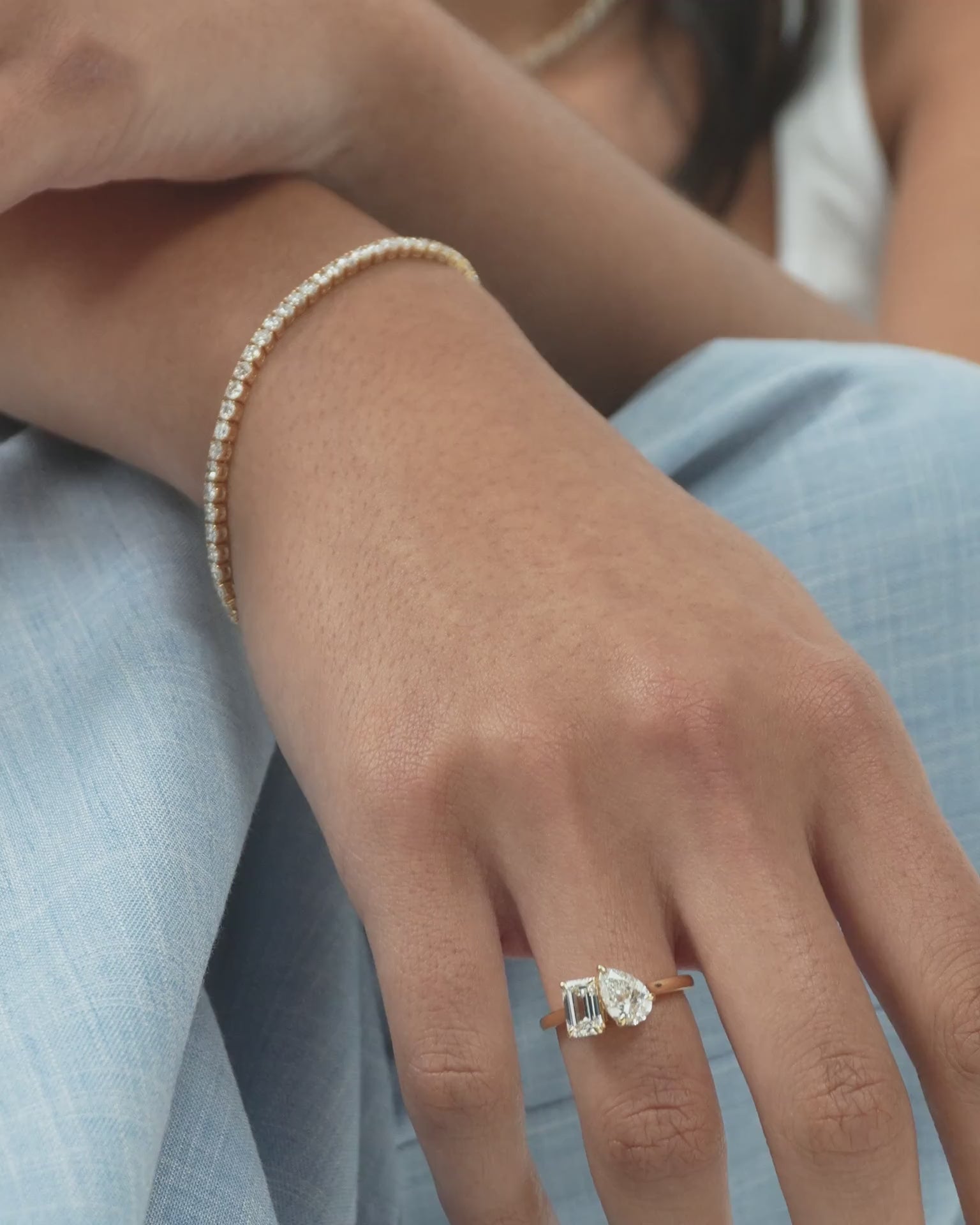 Close-up model wears Kinney Toi Et Moi pear emerald engagement ring in 18ct yellow gold