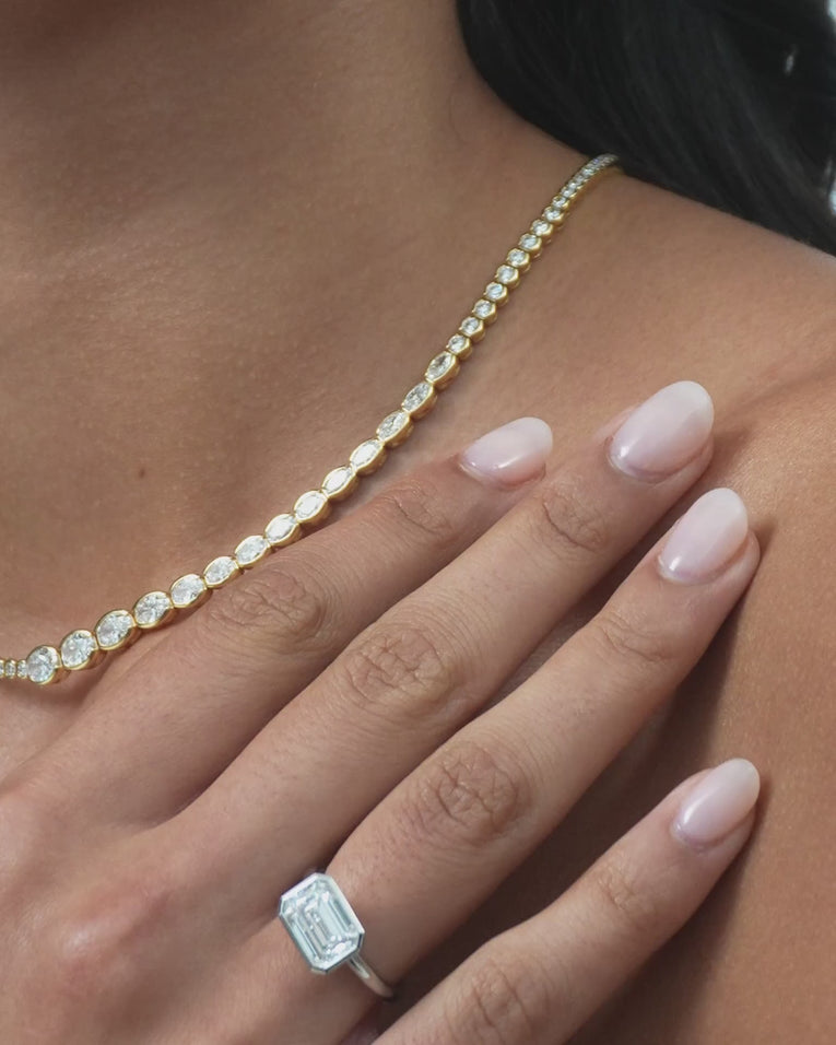 Model wears Rowan emerald cut solitaire bezel East-West engagement ring in 18ct white gold
